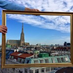 Hands hold picture frame aloft in sky to enclose silhouette of St. Stephen's Cathedral in Vienna